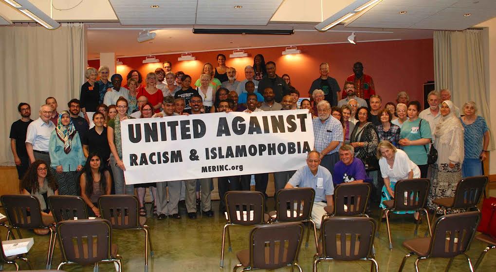 conference attendees gather around sign "United Against Racism & Islamophobia"