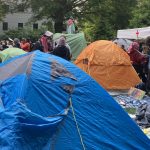 Palestine protester tents on the lawn of George Washington University's lawn with a statue wearing a flag in the background.